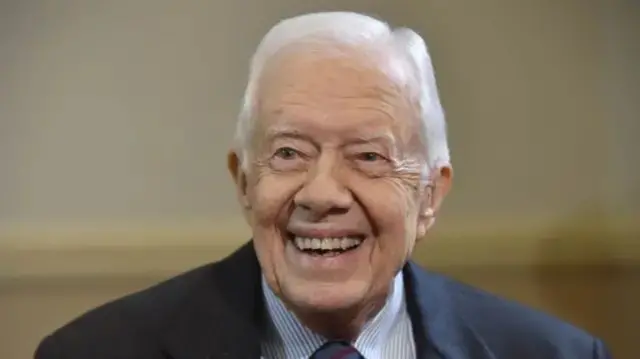 A file photo of Jimmy Carter in 2016. He is smiling and wearing a suit