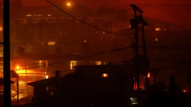 View of buildings on a hill with red haze covering the scene and powerlines in the foreground
