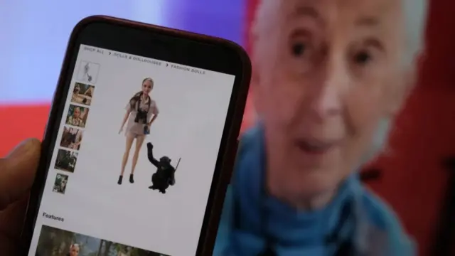 A person holding a phone that has on it a picture of the Goodall barbie next to a chimp against a white background. In the background of this is a picture of Goodall.