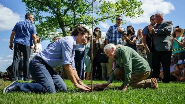 Justin Trudeau and Jane Goodall crouched down on the grass together.