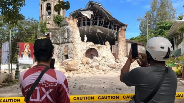 People take pictures in front of a damaged church in the aftermath of an earthquake in Bogo city, Cebu island