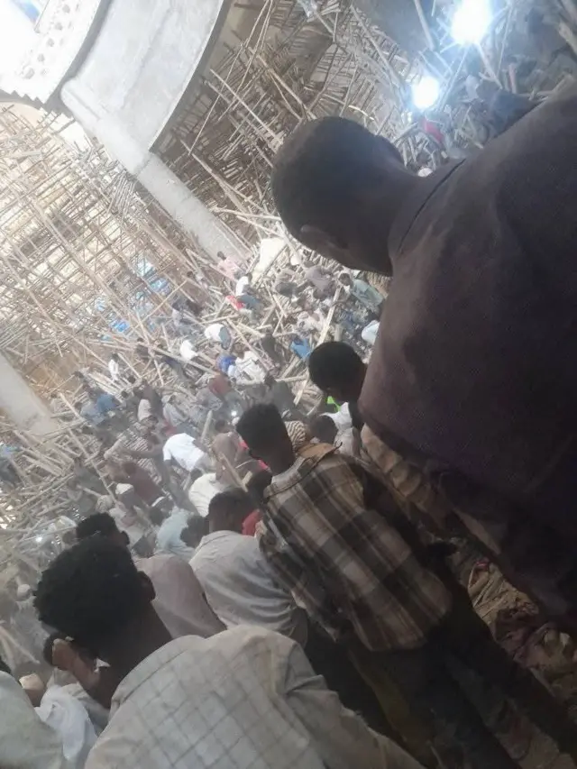 A crowd of people looking at collapsed scaffolding, while dozens of people search through the wooden scaffolding