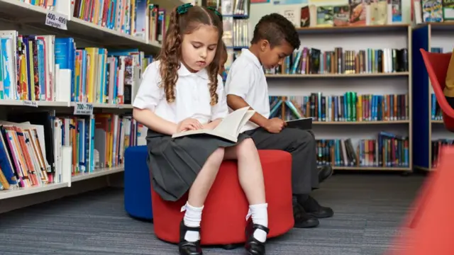 Young children in school uniform sitting in a library reading books
