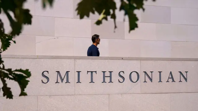 A man walks along the side of a building with a sign reading "Smithsonian"