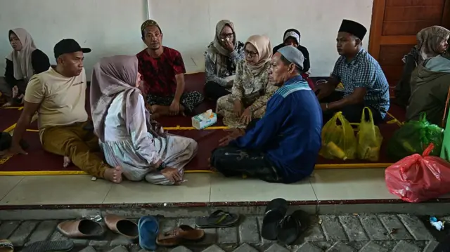 People sit in a circle on a mat on the ground