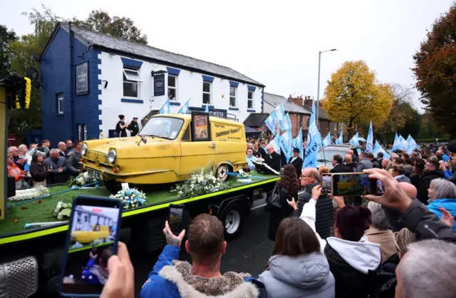 A truck carrying The Trotters' car from the show Only Fools and Horses is followed by a car carrying the coffin of former boxer Ricky Hatton