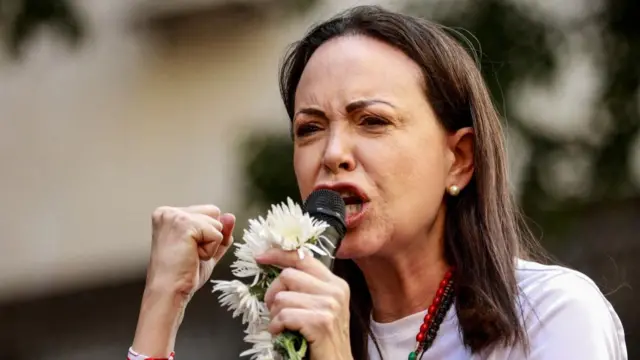 Maria Corina Machado speaking into a microphone with fist clenched