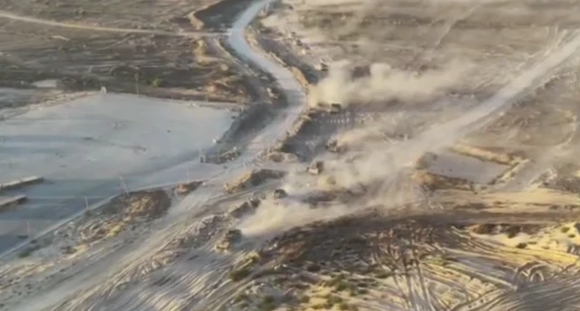 Multiple vehicles moving across a sandy terrain from above