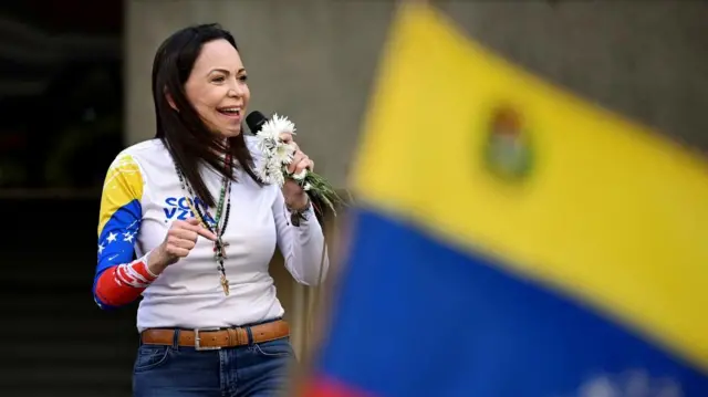 Venezuelan opposition leader Maria Corina Machado addresses supporters. She is smiling and holding a mic.