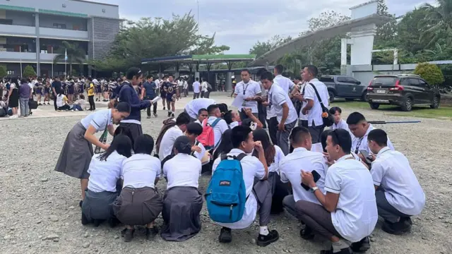 Students squatting down on the ground outside of a building