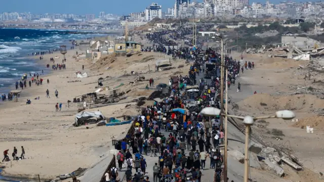 A wide-shot view of hundreds of Palestinians walking on a road near a beach in Gaza.