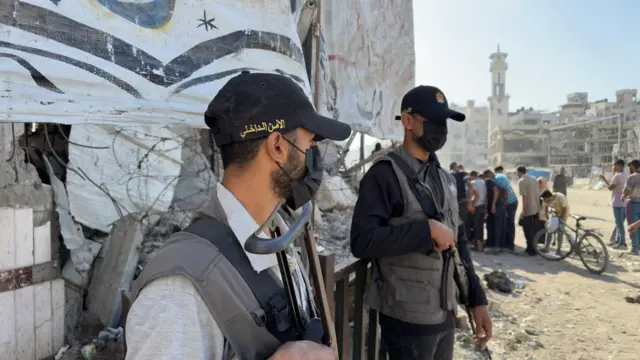 Two men wear masks and turn to the side as they hold guns