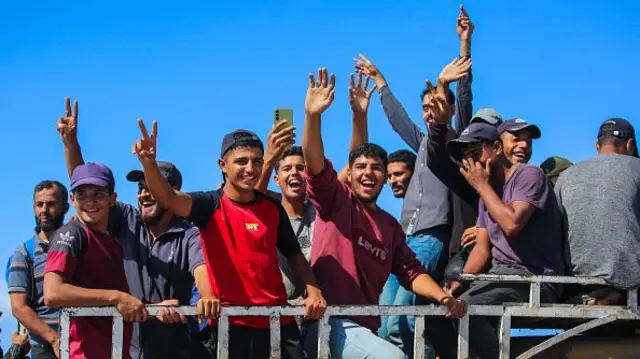 A group of boys on the back of a truck raise their hands in celebration