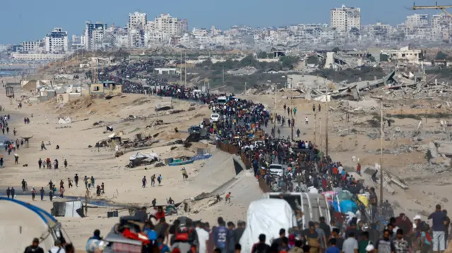 Thousands of Gaza walk down a path next to a beach. Debris and rubble litters the ground next to the road.