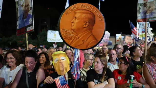 A large crowd, people hold a large coin that says Donald Trump Nobel Peace Prize.
