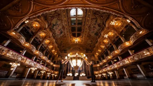 Staff getting the Tower Ballroom in Blackppol ready for performance. A man and a woman, dressed all in black, hang a chandler.