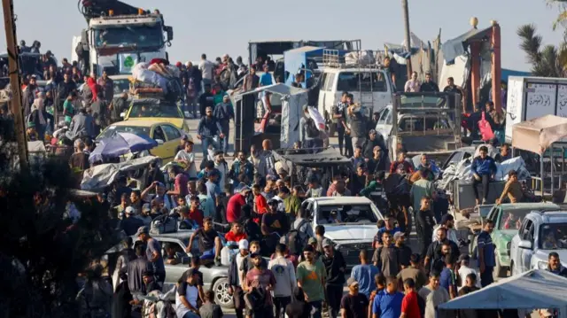 Crowds of people make their way along a road up to the north of Gaza. Many are on foot and are walking between vehicles carrying their belongings.