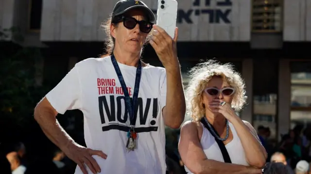 A woman, wearing a "Bring them home now!" shirt, holds a phone at "Hostages Square", after a ceasefire between Israel and Hamas in Gaza went into effect, in Tel Aviv, Israel