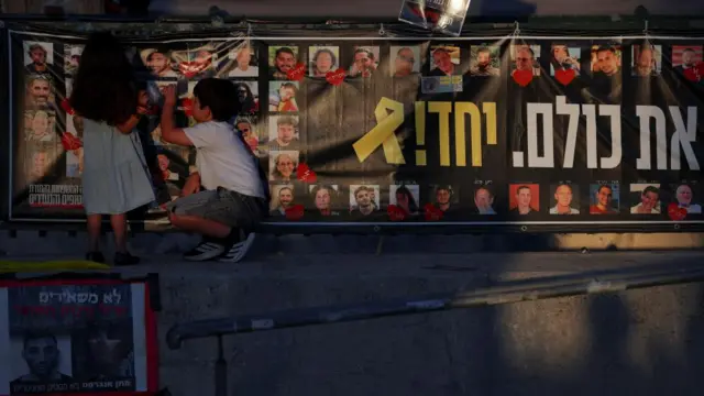 Children stand next to a banner with photos of hostages at "Hostages Square", after a ceasefire between Israel and Hamas in Gaza