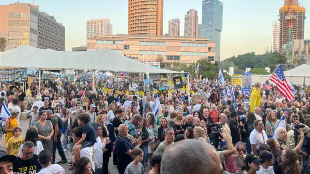 Large crowds assemble in Hostage Square in Tel Aviv in the late afternoon. Some people in the far right of the frame are holding two US flags, while others hold placards with pictures of the hostages or Israeli flags