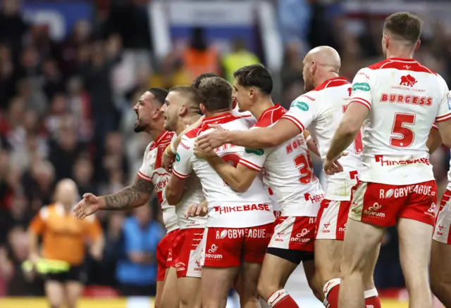 Hull KR players, wearing red and white shirts, red shorts and red socks celebrate with arms around each other.