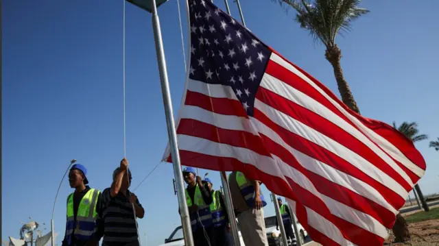 Workers hoist up a US flag on a pole during preparations for Donald Trump's arrival in Sharm El-Sheikh