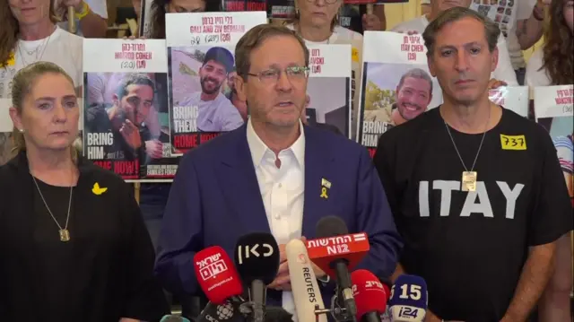 Sara Herzog (L) stands next to her husband, Israeli President Isaac Herzog, as he delivers a speech surrounded by the family and friends of hostages holding placards with their pictures