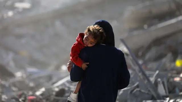 A Palestinian mother carrying her child walks among the rubble of destroyed buildings