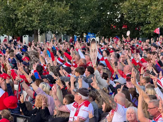 A crowd of people in the city centre holding three fingers up in the air