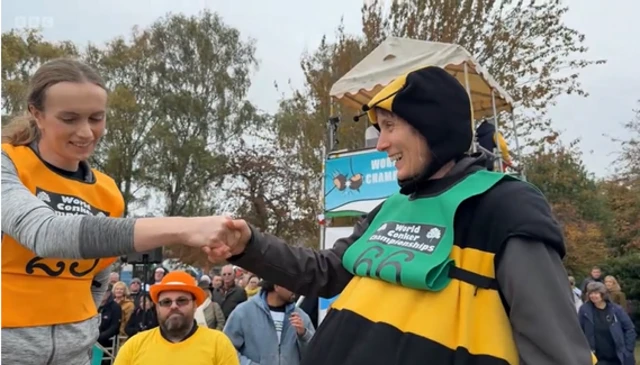 A smiling woman dressed as a bumble bee shakes hands with a woman in a grey top
