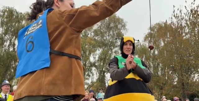 A woman in a bee costume takes aim with a conker as a woman in a brown jacket hold up a conker