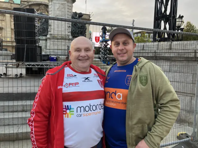Two men wearing rugby shirts are standing in Hull City Centre. Behind them is a metal fence.