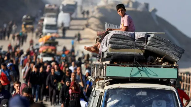A Palestinian boy sits atop of a vehicle carrying belongings, as he and other Palestinians, who were displaced to the southern part of Gaza at Israel's order during the war, make their way along a road as they return to the north