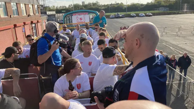 The top deck of a bus. Players with white T-shirts are sitting wearing sun glasses and holding bottles of beer.