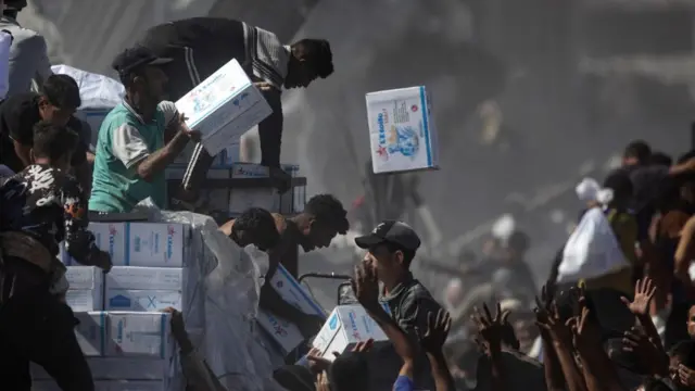 White boxes are thrown into a big crowd from an aid truck