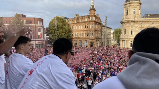 Hull players standing on the balcony of Hull City Hall looking out to a crowd of people in red and white shirts