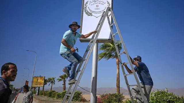 Two men stand on a ladder on a road in Sharm El-Sheikh, Egypt, one holds hammer as a sign is being put up.