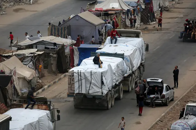Humanitarian aid trucks entering the Nusseirat refugee camp in central Gaza Strip, drive past tents used as temporary shelters by displaced Palestinians, on October 12, 2025.