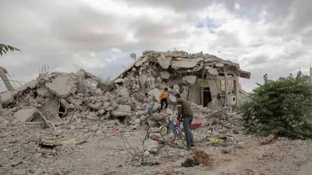 A man and two boys search for belongings in the rubble of a house
