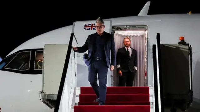 Starmer descends the stairs of a plane with a UK flag on the inside of the door