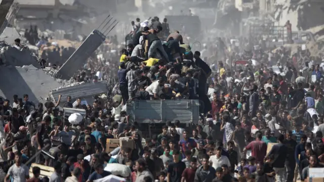 A huge number of people surround an aid lorry which has arrived in Khan Younis, several people have climbed onto it.