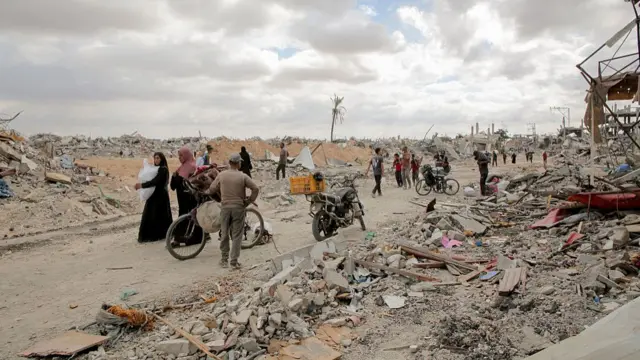 Several people stand on the remains of a road with large piles of rubble on either side