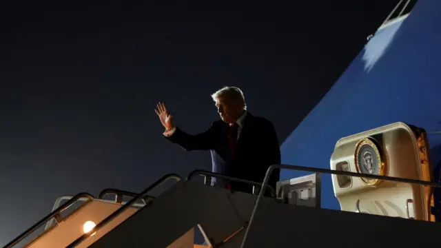 Trump waves from the top of the stairs before he boards Air Force One