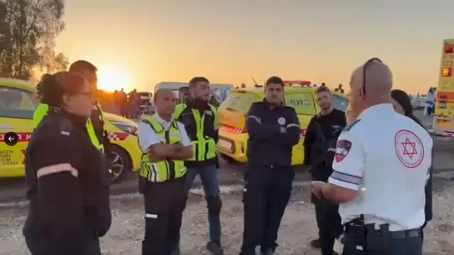 Emergency workers in uniform gather, surrounded by neon yellow emergency vehicles