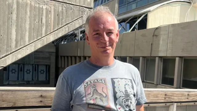 Man wearing a t-shirt picturing a tiger and scorpion smiles to camera