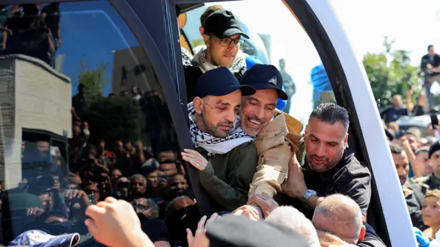 Men hold hands of a crowd  surrounding a bus of people smiling