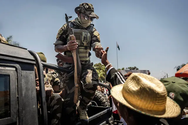 A member of a Malagasy Army unit riding on a patrol vehicle exchanges a fist bump with a civilian as residents gather for a civil society rally outside City Hall in Antananarivo, on October 13, 2025. Soldiers and security forces joined hundreds celebrating in Madagascar's capital on October 13, 2025, hours before President Andry Rajoelina was due to address the nation following weeks of protests and growing calls for his resignation. (Photo by Luis TATO / AFP) (Photo by LUIS TATO/AFP via Getty Images)