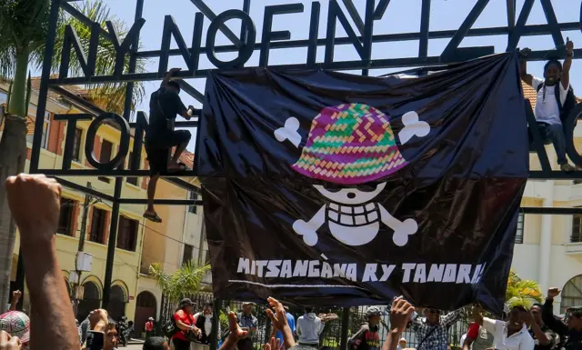 TOPSHOT - Residents gather as youngsters hang a large banner featuring a Malagasy version of the logo of the popular Japanese manga One Piece, a symbol adopted by Gen Z protest movements worldwide, in front of City Hall in Antananarivo, on October 12, 2025. A mutinied army unit declared on October 12, 2025 that it was taking control of all Madagascar military forces as President Andry Rajoelina said an "attempt to seize power illegally" was under way.The CAPSAT contingent of administrative and technical officers joined thousands of protesters in the city centre on October 11, 2025 in a major shift in a more than two-week anti-government protest movement. (Photo by Luis TATO / AFP) (Photo by LUIS TATO/AFP via Getty Images)