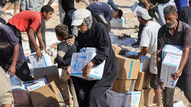 Starving Palestinians carry white boxes of food aid in the Gaza strip