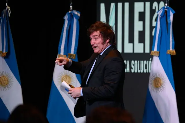 Milei pointing to supporters in front of Argentine flags